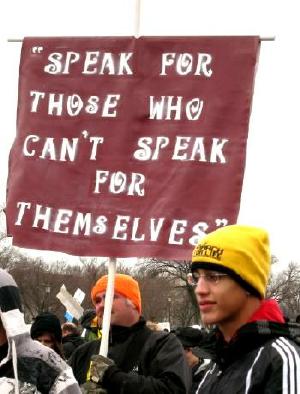 Two men with banner that says, 'Speak for Those Who Can't 
Speak for Themselves'